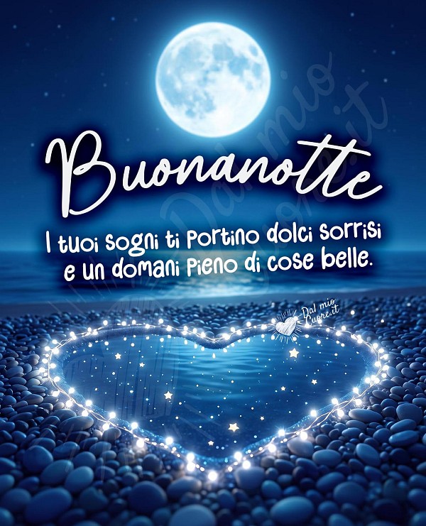 Immagine notturna di un paesaggio marino con una grande luna piena che splende alta nel cielo scuro. Sulla spiaggia di ciottoli, un grande cuore è delineato da una fila di luci bianche brillanti, con piccole stelle e punti luce che fluttuano all'interno del cuore stesso. Le onde del mare si infrangono dolcemente sulla riva. Al centro dell'immagine, su un riquadro beige, spicca la scritta 'Buonanotte', in un carattere più piccolo, è presente la frase 'i tuoi sogni ti portino dolci sorrisi e un domani pieno di cose belle.' Il cielo e il mare sono di un blu notte intenso, mentre la luna è di un bianco brillante.